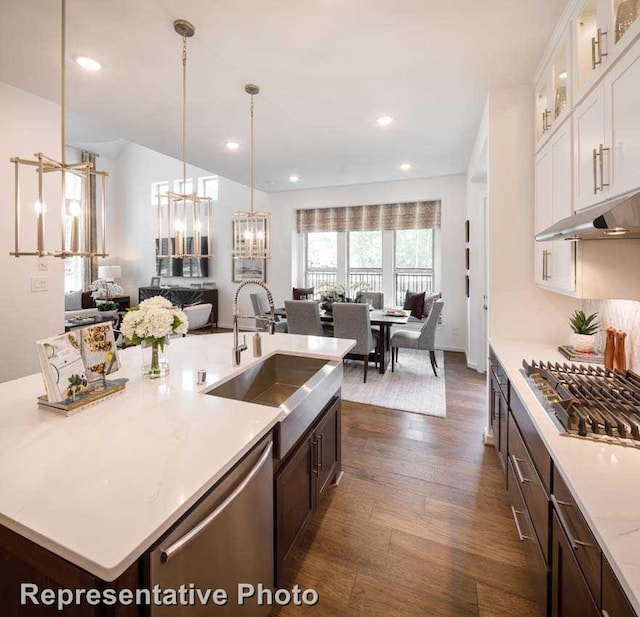 kitchen featuring appliances with stainless steel finishes, hanging light fixtures, sink, dark wood-type flooring, and a kitchen island with sink