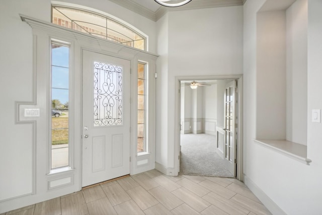 carpeted foyer entrance featuring a wealth of natural light, crown molding, and ceiling fan