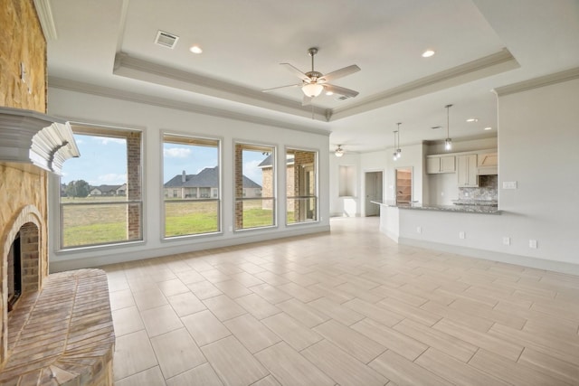 unfurnished living room featuring ceiling fan, a raised ceiling, a fireplace, and crown molding