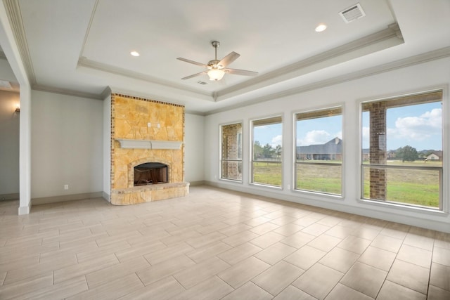 unfurnished living room featuring a raised ceiling, ceiling fan, a fireplace, and ornamental molding