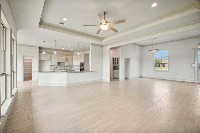 unfurnished living room with ceiling fan with notable chandelier, ornamental molding, sink, and a tray ceiling