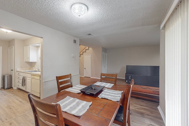 dining area with a textured ceiling, sink, and light wood-type flooring