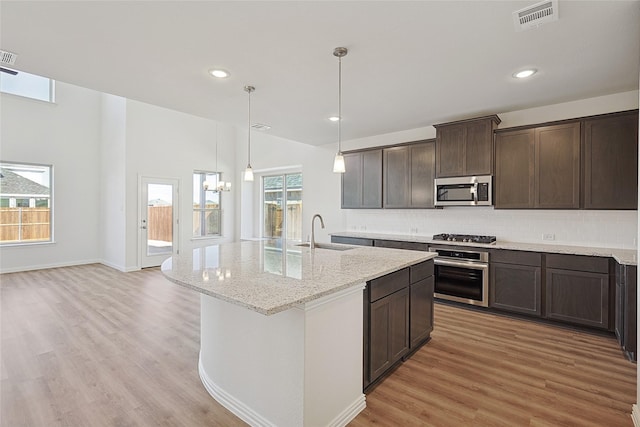 kitchen with dark brown cabinetry, appliances with stainless steel finishes, sink, light stone counters, and a center island with sink