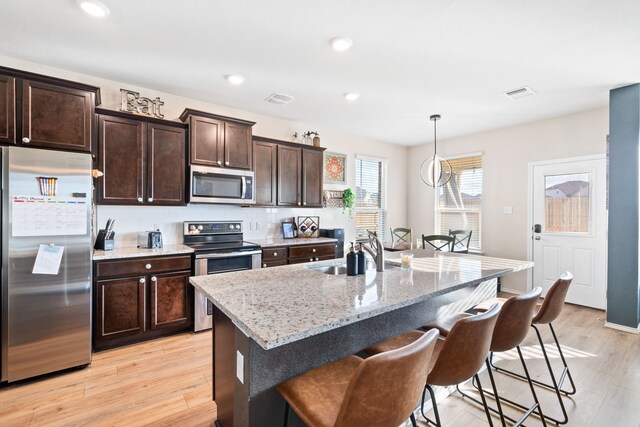 kitchen featuring light stone countertops, sink, hanging light fixtures, stainless steel appliances, and an island with sink