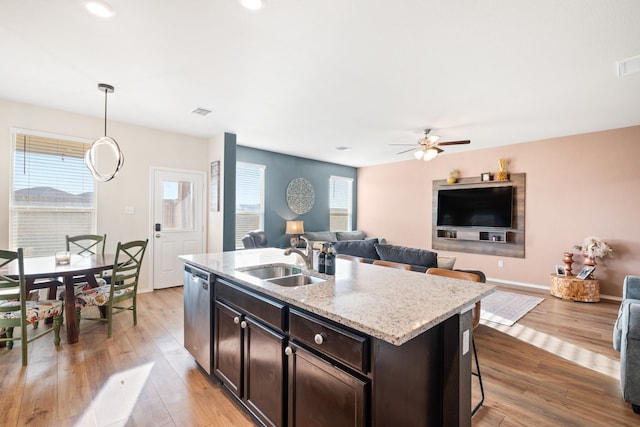 kitchen with light stone countertops, a kitchen island with sink, sink, pendant lighting, and dishwasher