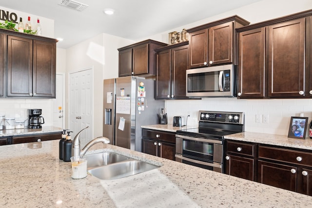 kitchen featuring light stone countertops, appliances with stainless steel finishes, backsplash, and dark brown cabinets