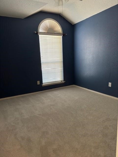 carpeted empty room featuring a textured ceiling, lofted ceiling, and ceiling fan