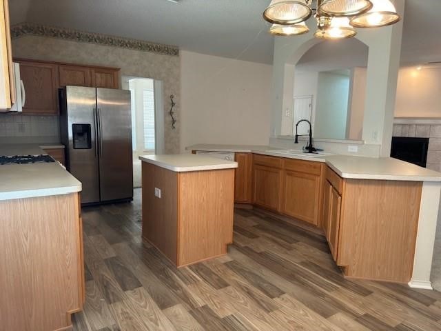 kitchen featuring wood-type flooring, kitchen peninsula, sink, stainless steel fridge with ice dispenser, and a kitchen island