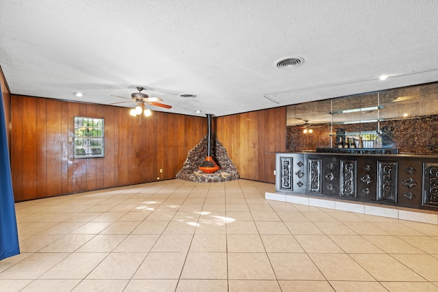 interior space with a textured ceiling, wooden walls, ceiling fan, and light tile patterned flooring