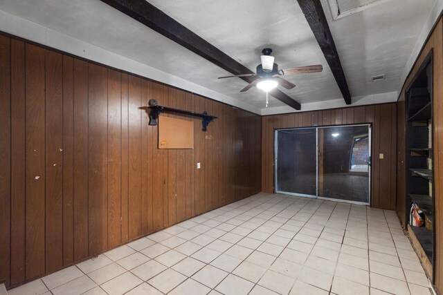 spare room featuring wood walls, beamed ceiling, light tile patterned floors, and ceiling fan