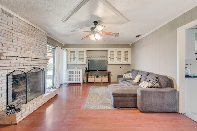 living room featuring ornamental molding, ceiling fan, a textured ceiling, hardwood / wood-style floors, and a brick fireplace