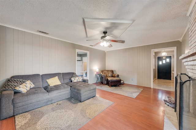 living room featuring a fireplace, wood-type flooring, wooden walls, and a textured ceiling