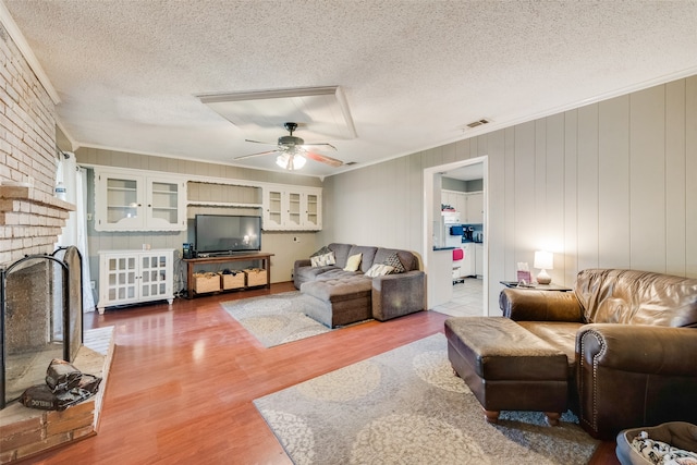 living room featuring a brick fireplace, hardwood / wood-style floors, a textured ceiling, and ceiling fan