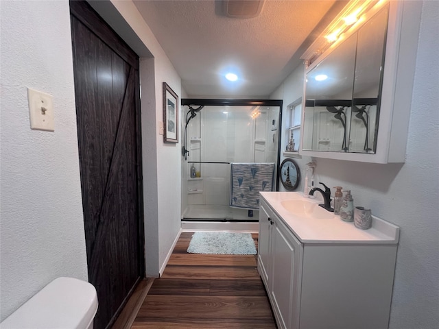 bathroom with wood-type flooring, vanity, walk in shower, toilet, and a textured ceiling