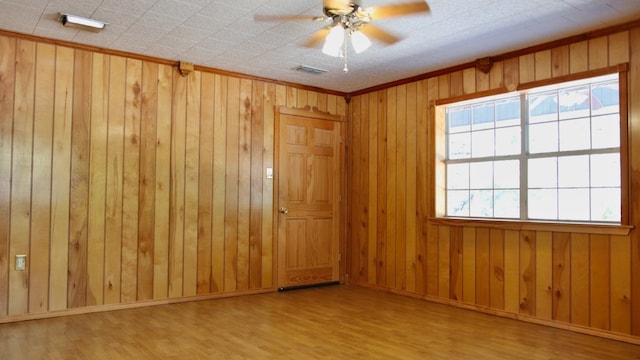 empty room with ceiling fan, wood walls, and light wood-type flooring