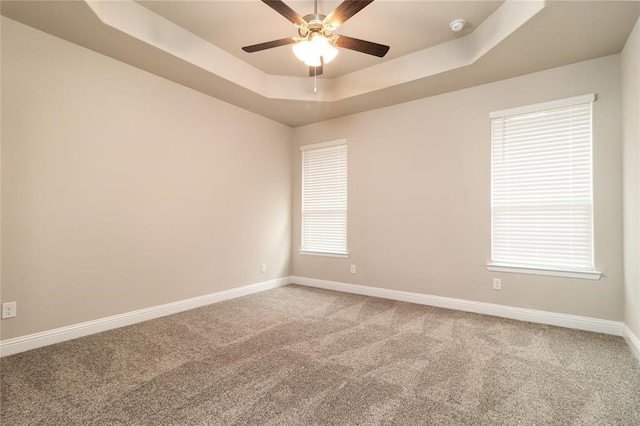 carpeted spare room with a wealth of natural light, ceiling fan, and a tray ceiling