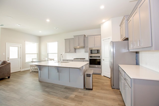 kitchen with stainless steel appliances, sink, a kitchen bar, an island with sink, and gray cabinetry