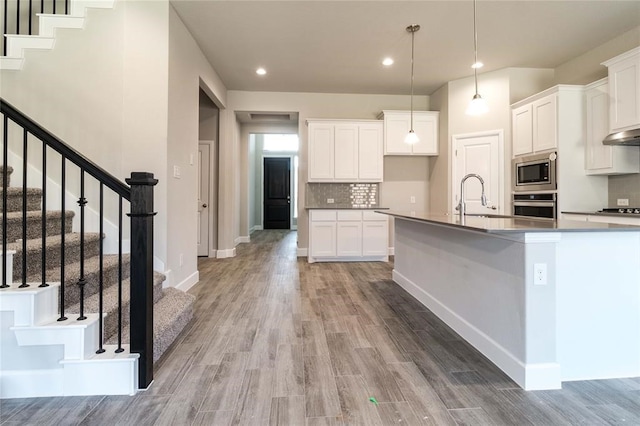 kitchen featuring stainless steel appliances, sink, hanging light fixtures, hardwood / wood-style floors, and white cabinets