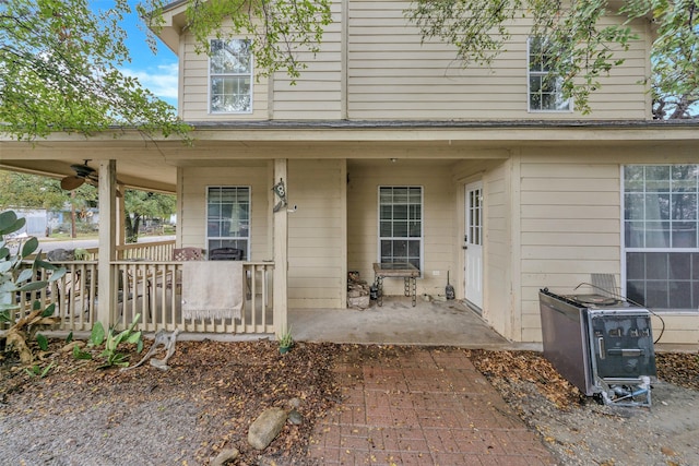 view of exterior entry with ceiling fan, covered porch, and a patio