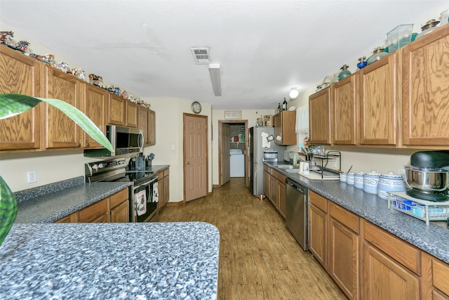 kitchen featuring washer / clothes dryer, sink, light hardwood / wood-style flooring, and appliances with stainless steel finishes