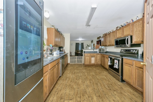 kitchen featuring kitchen peninsula, stainless steel appliances, light hardwood / wood-style flooring, and sink