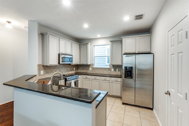 kitchen featuring dark stone counters, backsplash, kitchen peninsula, and stainless steel appliances