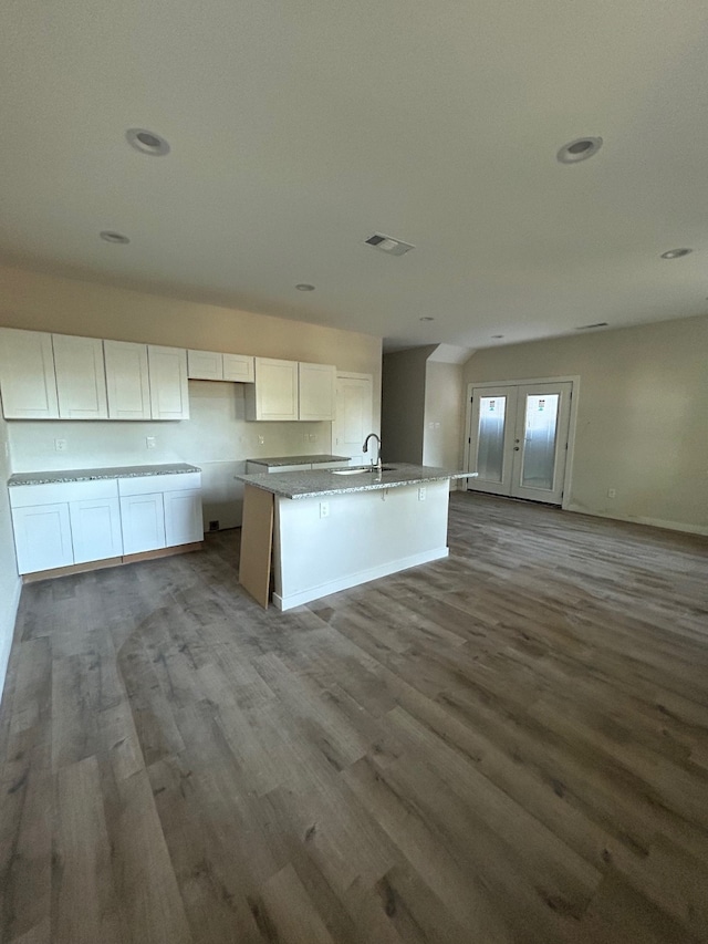 kitchen with light stone counters, a center island with sink, white cabinetry, sink, and hardwood / wood-style flooring