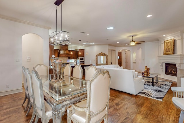 dining space featuring hardwood / wood-style floors, a fireplace, crown molding, and ceiling fan with notable chandelier