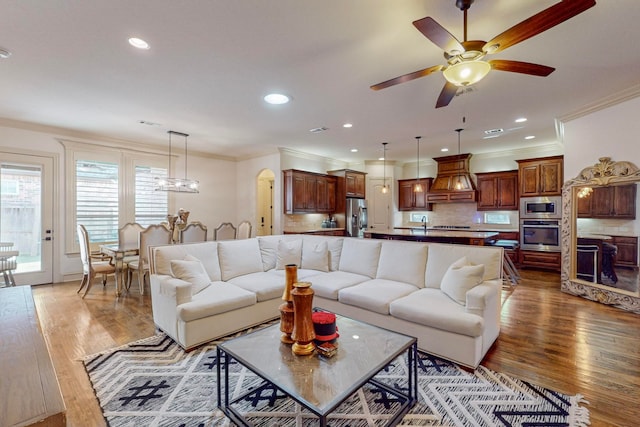 living room featuring hardwood / wood-style flooring, ceiling fan with notable chandelier, and crown molding