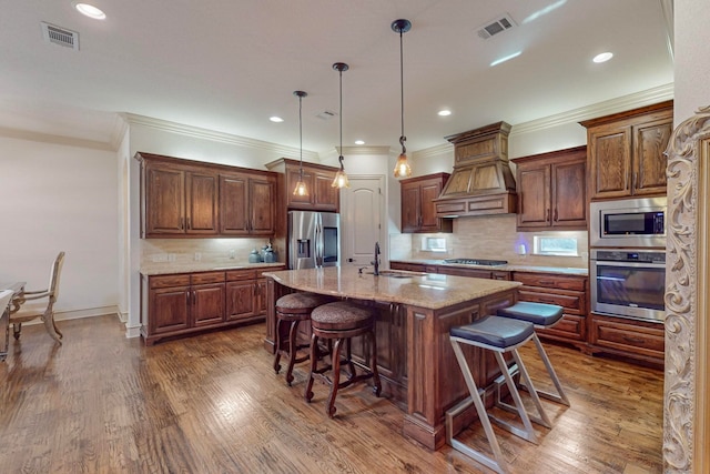 kitchen featuring appliances with stainless steel finishes, light stone countertops, pendant lighting, dark wood-type flooring, and a kitchen island with sink