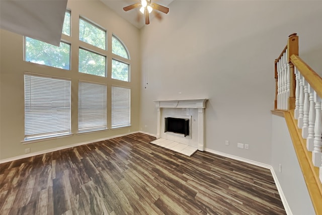 unfurnished living room featuring dark wood-type flooring, a high ceiling, ceiling fan, and a tile fireplace