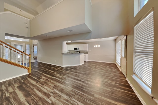 unfurnished living room featuring a towering ceiling, dark hardwood / wood-style flooring, and plenty of natural light