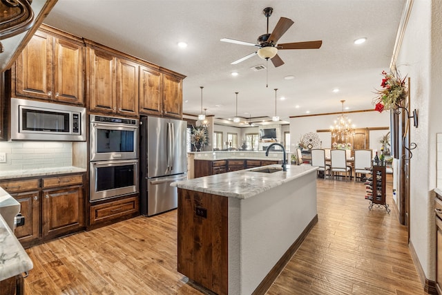 kitchen featuring a center island with sink, light hardwood / wood-style flooring, sink, pendant lighting, and appliances with stainless steel finishes