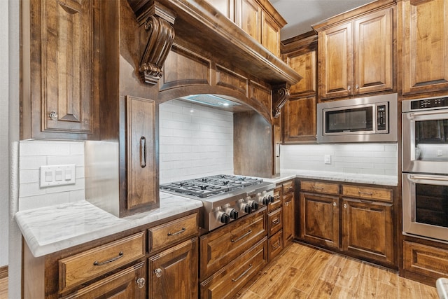 kitchen with tasteful backsplash, light wood-type flooring, appliances with stainless steel finishes, and premium range hood