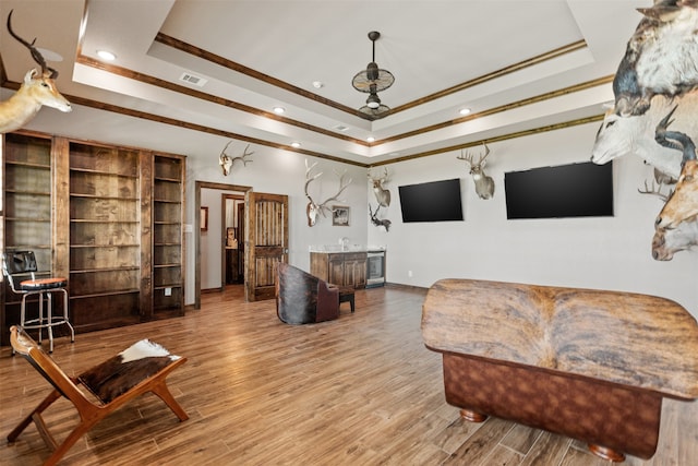 living room featuring hardwood / wood-style floors, indoor bar, crown molding, and a tray ceiling