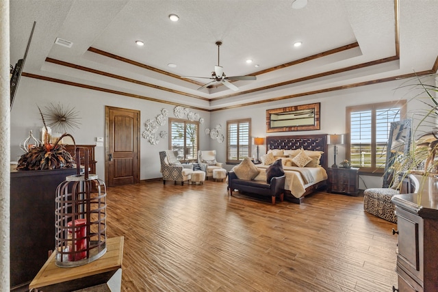 bedroom with wood-type flooring, multiple windows, and a raised ceiling