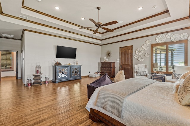 bedroom with crown molding, hardwood / wood-style floors, ceiling fan, and a raised ceiling