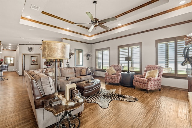 living room featuring hardwood / wood-style flooring, ceiling fan, crown molding, and a tray ceiling