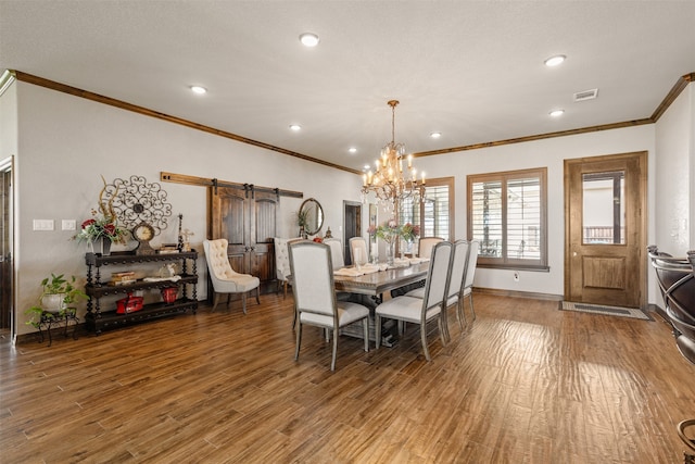 dining space with a barn door, hardwood / wood-style flooring, an inviting chandelier, and crown molding