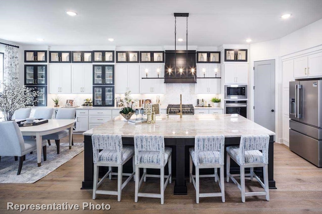 kitchen with hardwood / wood-style floors, hanging light fixtures, extractor fan, appliances with stainless steel finishes, and a large island with sink