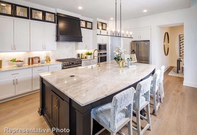 kitchen with high end appliances, premium range hood, decorative light fixtures, and a large island with sink