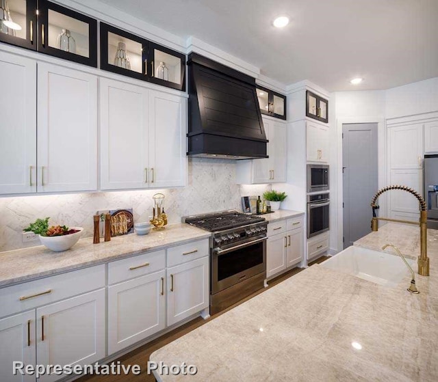 kitchen featuring stainless steel appliances, white cabinetry, sink, light stone countertops, and premium range hood