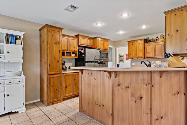 kitchen with a kitchen bar, light tile patterned floors, and stainless steel refrigerator