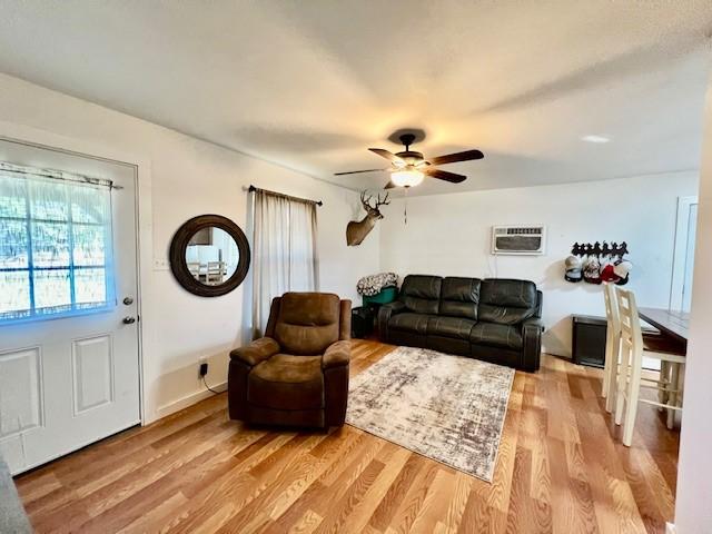 living room featuring a wall mounted AC, ceiling fan, and light hardwood / wood-style floors