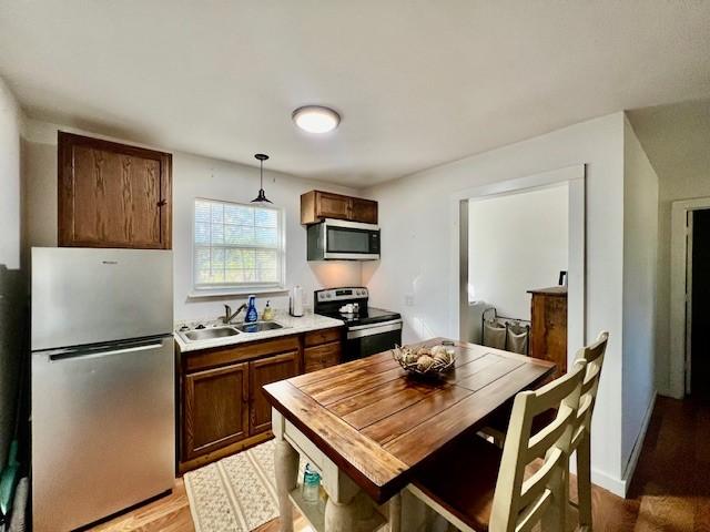 kitchen featuring hanging light fixtures, sink, stainless steel appliances, and light hardwood / wood-style flooring