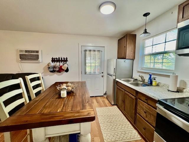 kitchen with hanging light fixtures, light hardwood / wood-style floors, appliances with stainless steel finishes, a wall mounted air conditioner, and sink