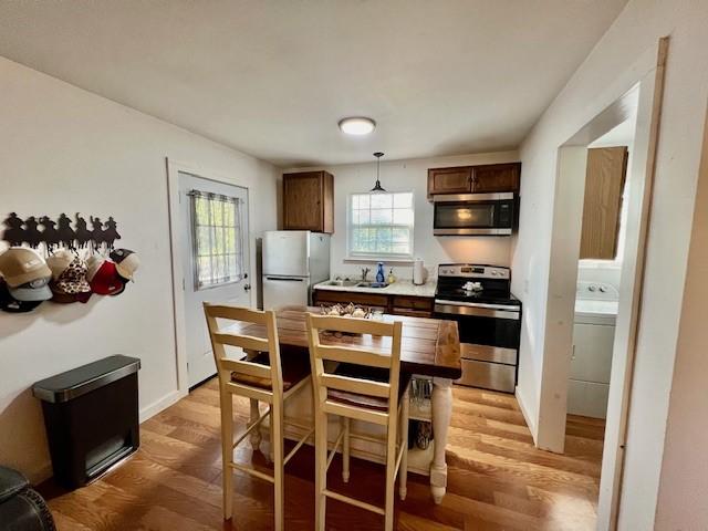 kitchen with decorative light fixtures, appliances with stainless steel finishes, washer / dryer, and light wood-type flooring