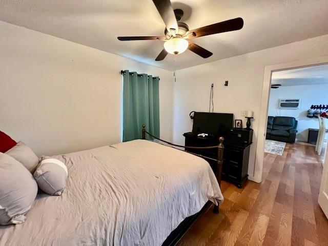 bedroom featuring a wall mounted AC, ceiling fan, and wood-type flooring