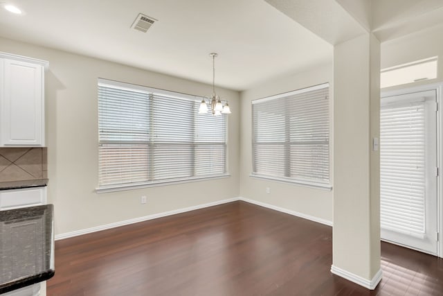 unfurnished dining area featuring dark wood-type flooring, a notable chandelier, and plenty of natural light