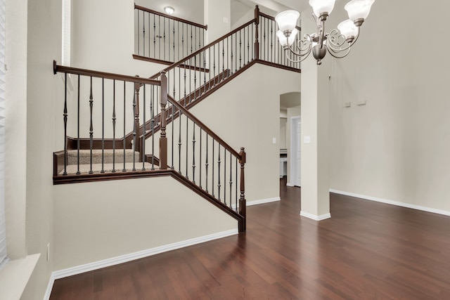 stairs with a towering ceiling, wood-type flooring, and a notable chandelier